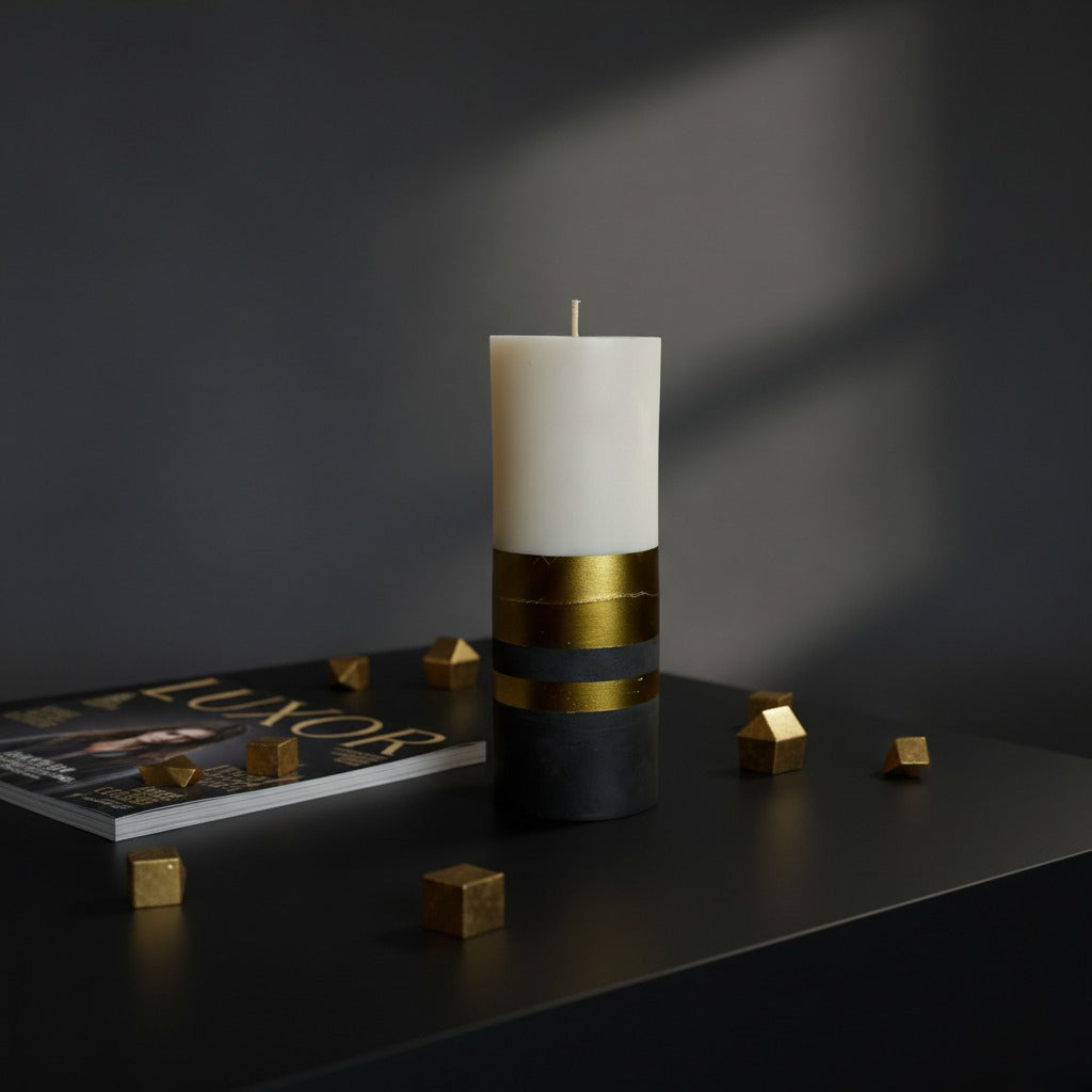 White candle with gold accents on a dark surface with geometric objects