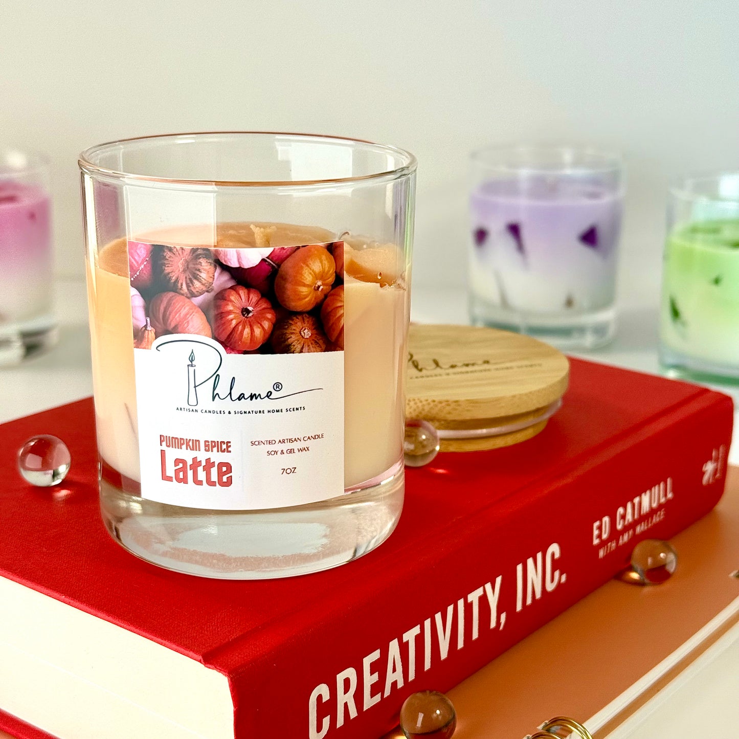 Candle labeled 'Pumpkin Spice Latte' on a red book with a blurred background