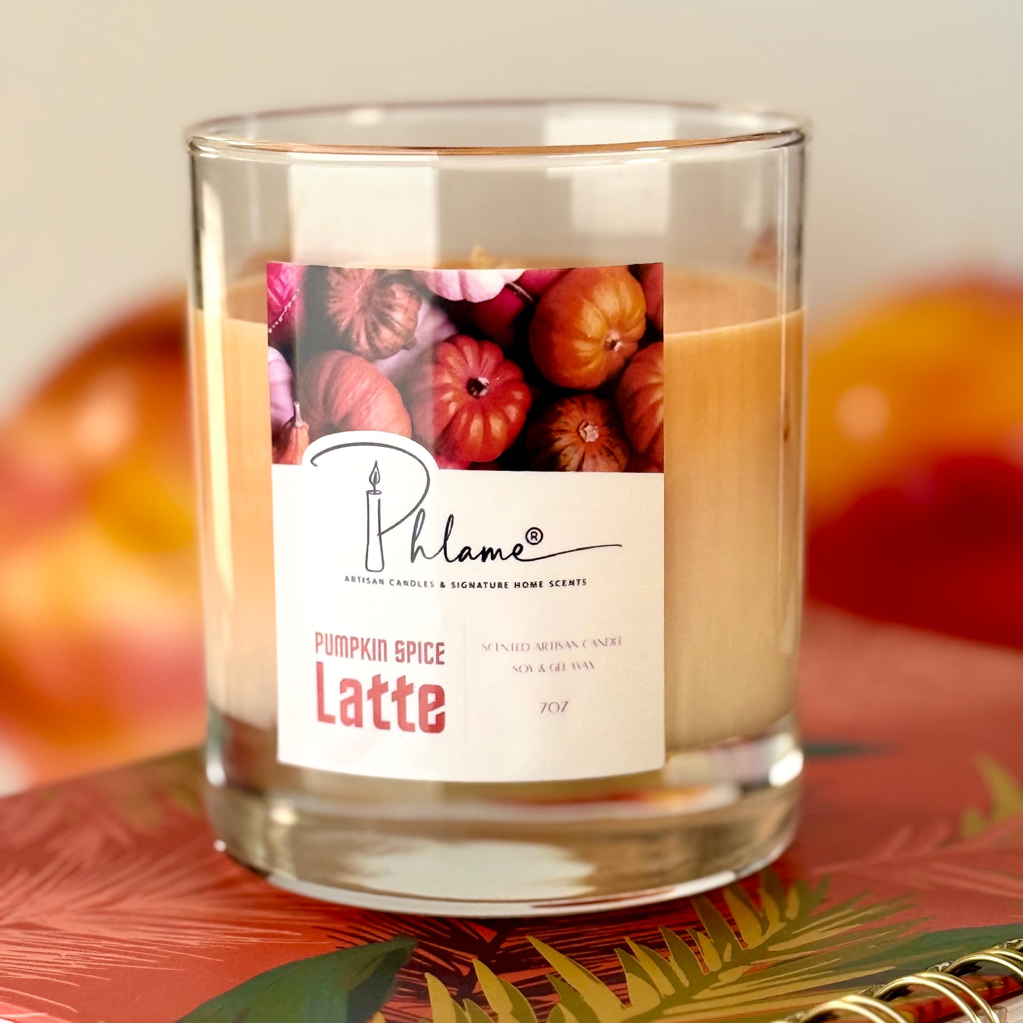 Candle labeled 'Pumpkin Spice Latte' by Phlame with a blurred background of pumpkins.