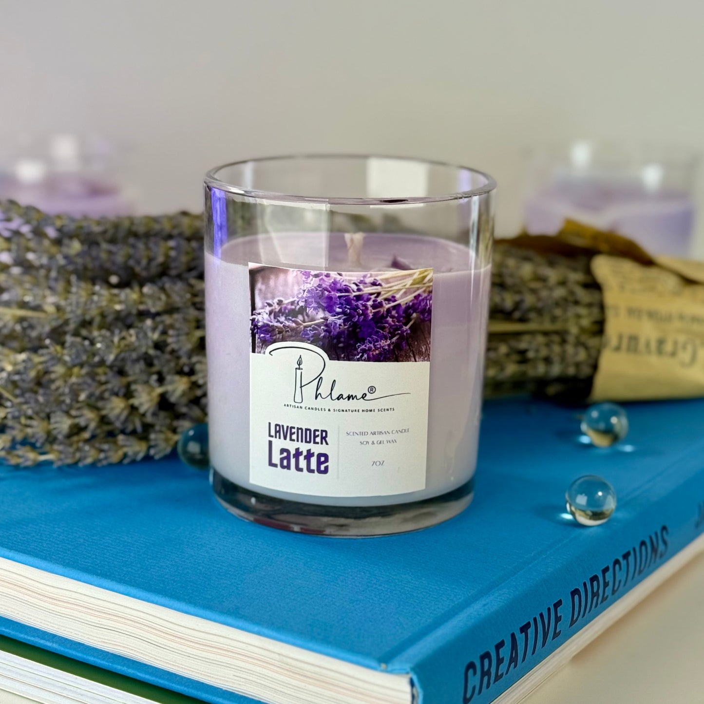 Candle labeled 'Lavender Latte' on a blue book with lavender flowers in the background