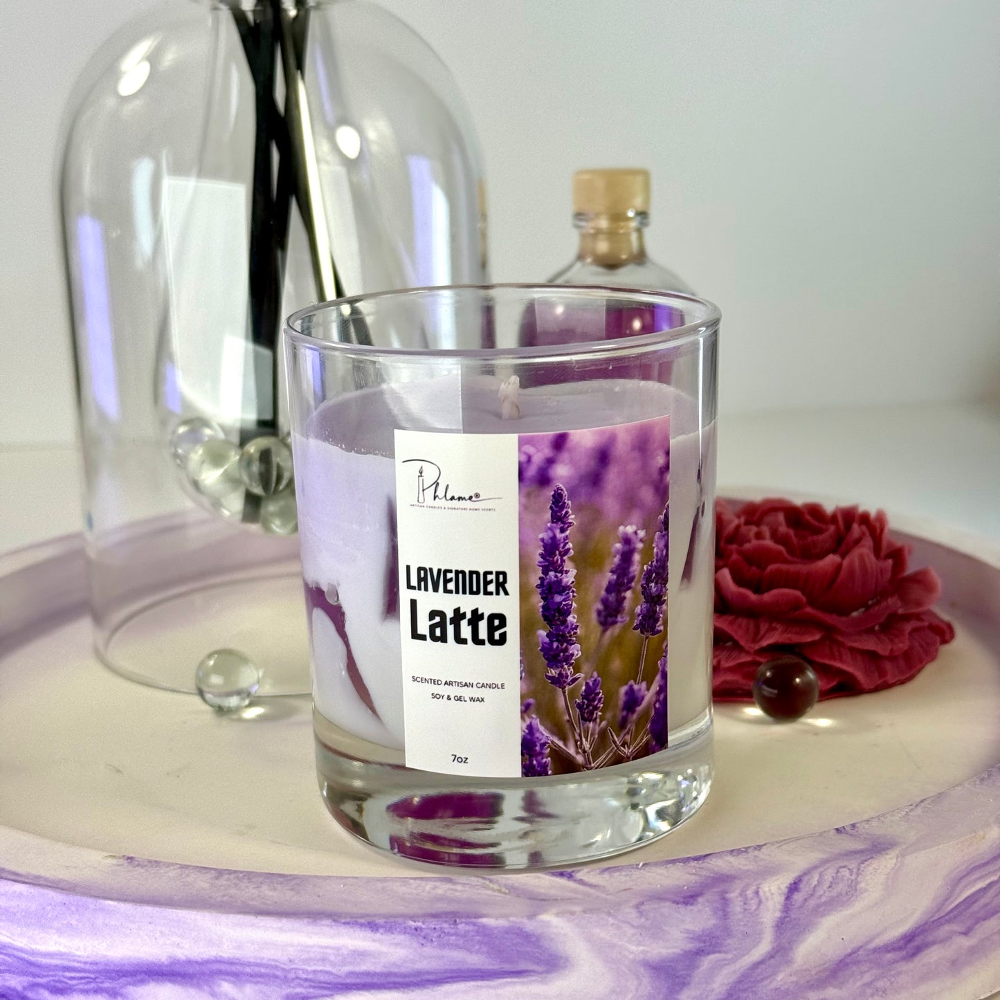 Glass candle labeled 'Lavender Latte' with a decorative bottle and flowers on a white surface.