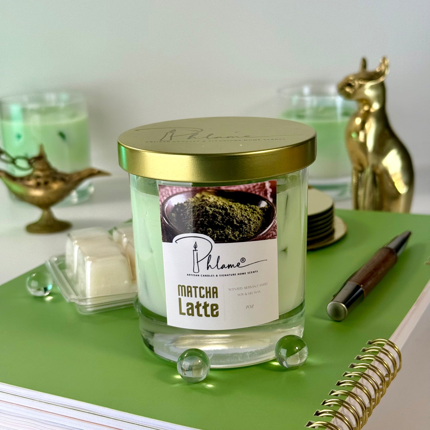 Matcha Latte candle in a glass jar with a gold lid on a green surface.