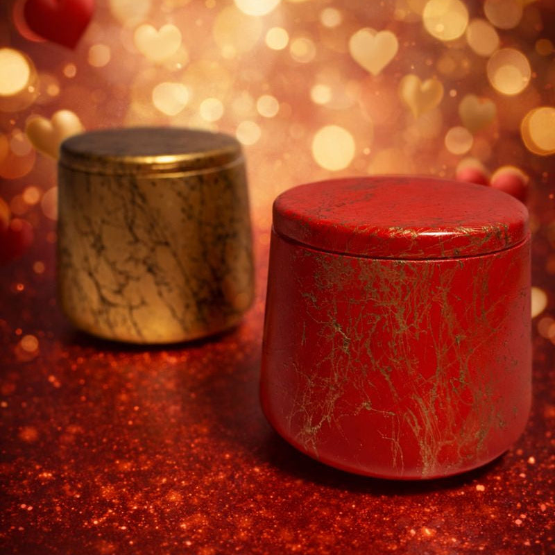 Two cylindrical containers, one gold and one red, on a glittery surface with heart-shaped lights in the background.