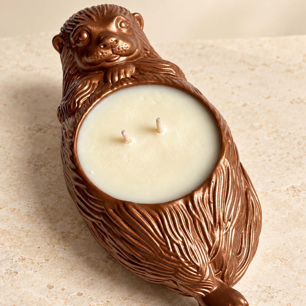 An otter-shaped candle holder shaped like a brown otter with a cream-colored wax candle inside, set against a light beige stone background.