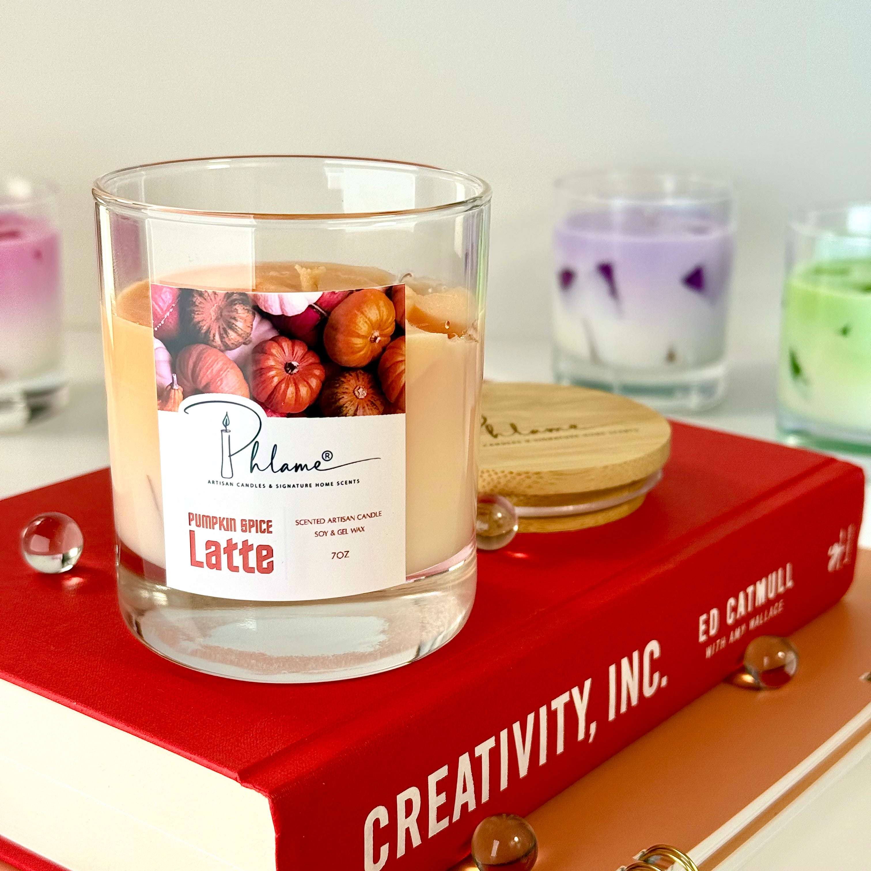 Candle labeled 'Pumpkin Spice Latte' on a red book with a blurred background