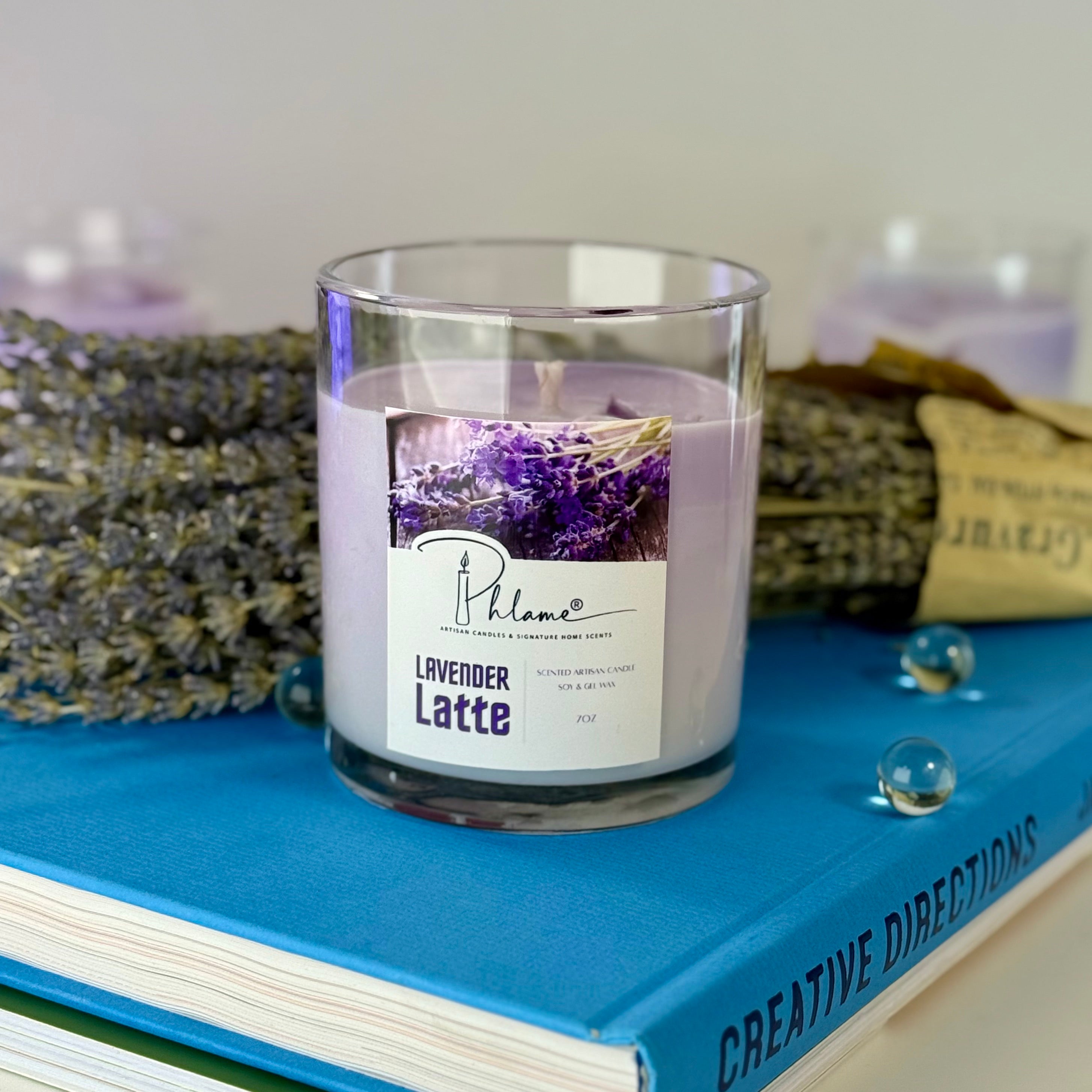 Candle labeled 'Lavender Latte' on a blue book with lavender flowers in the background