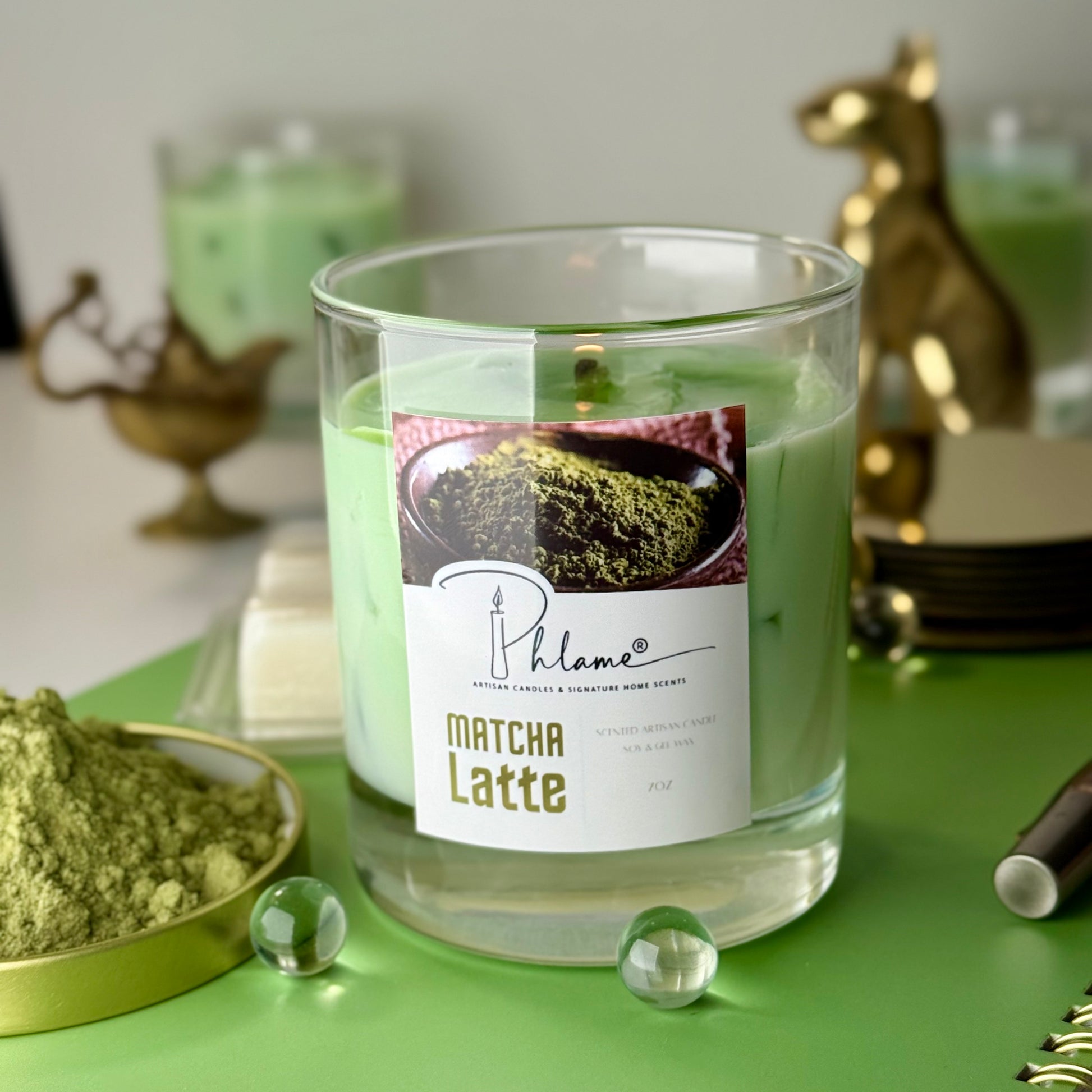 Matcha Latte candle with a label on a green surface, surrounded by matcha powder and decorative items.