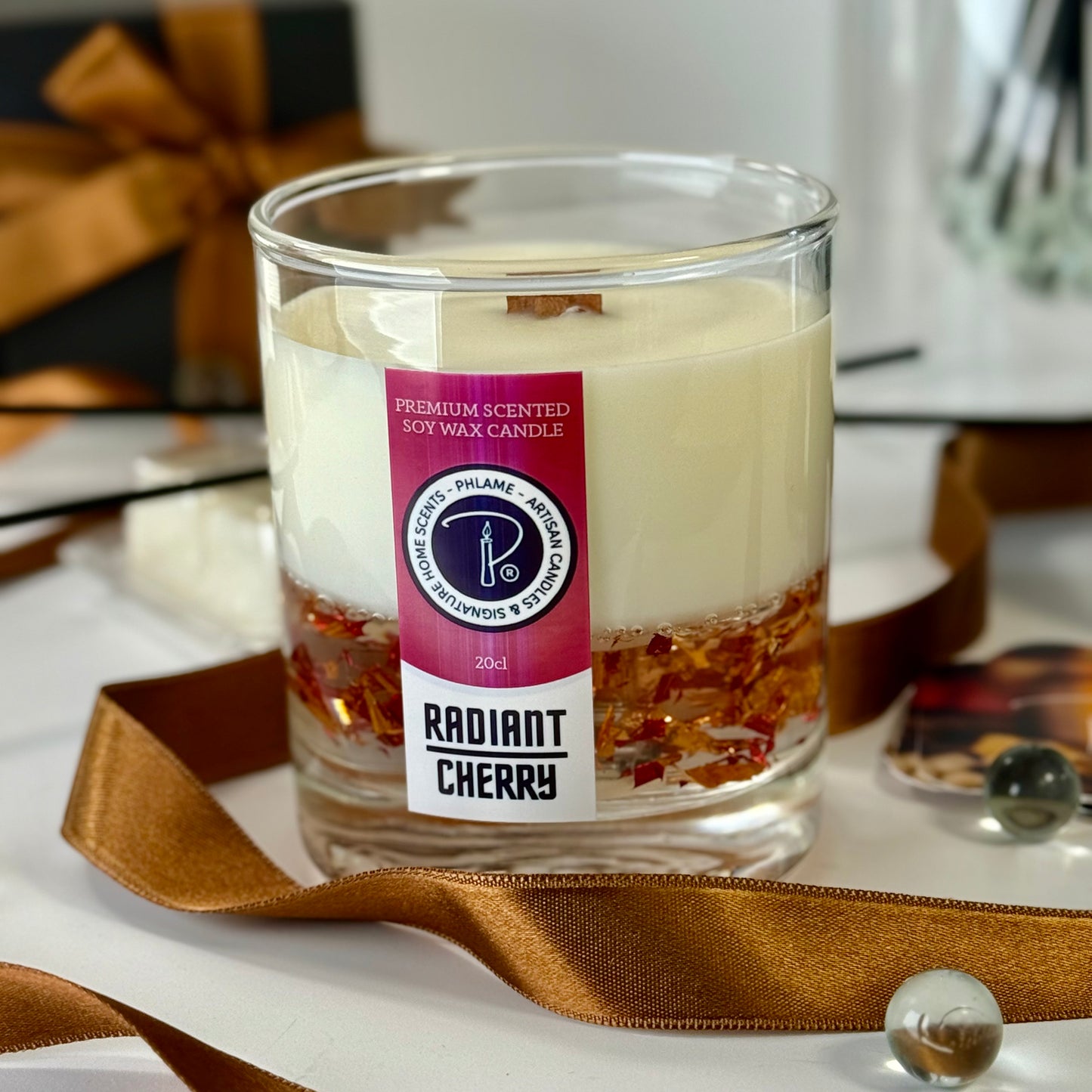 Candle labeled 'Radiant Cherry' with decorative ribbon and gift box in the background
