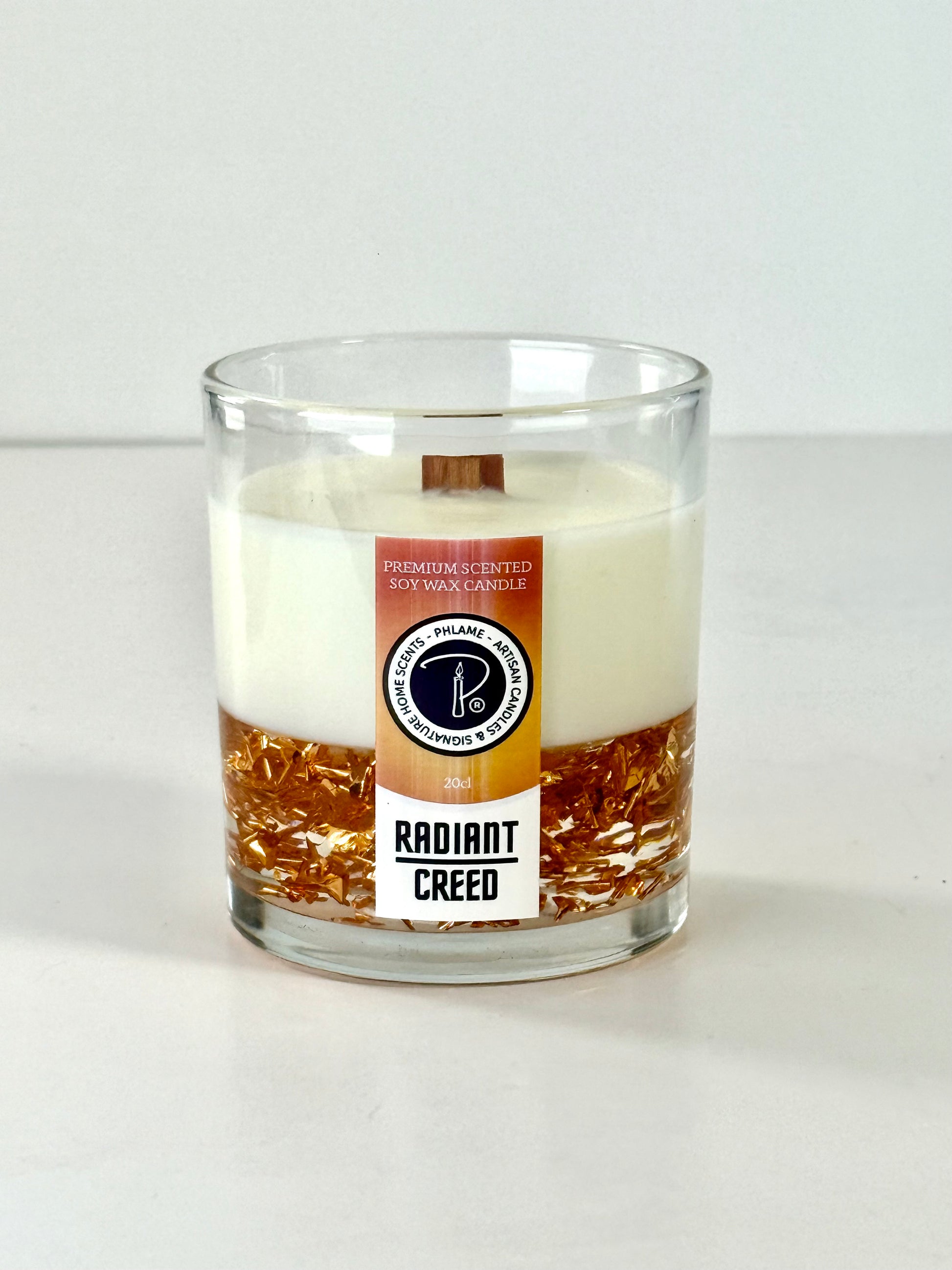 Radiant Creed candle with layered wax and wooden wick in black gift box, styled with citrus and spices.