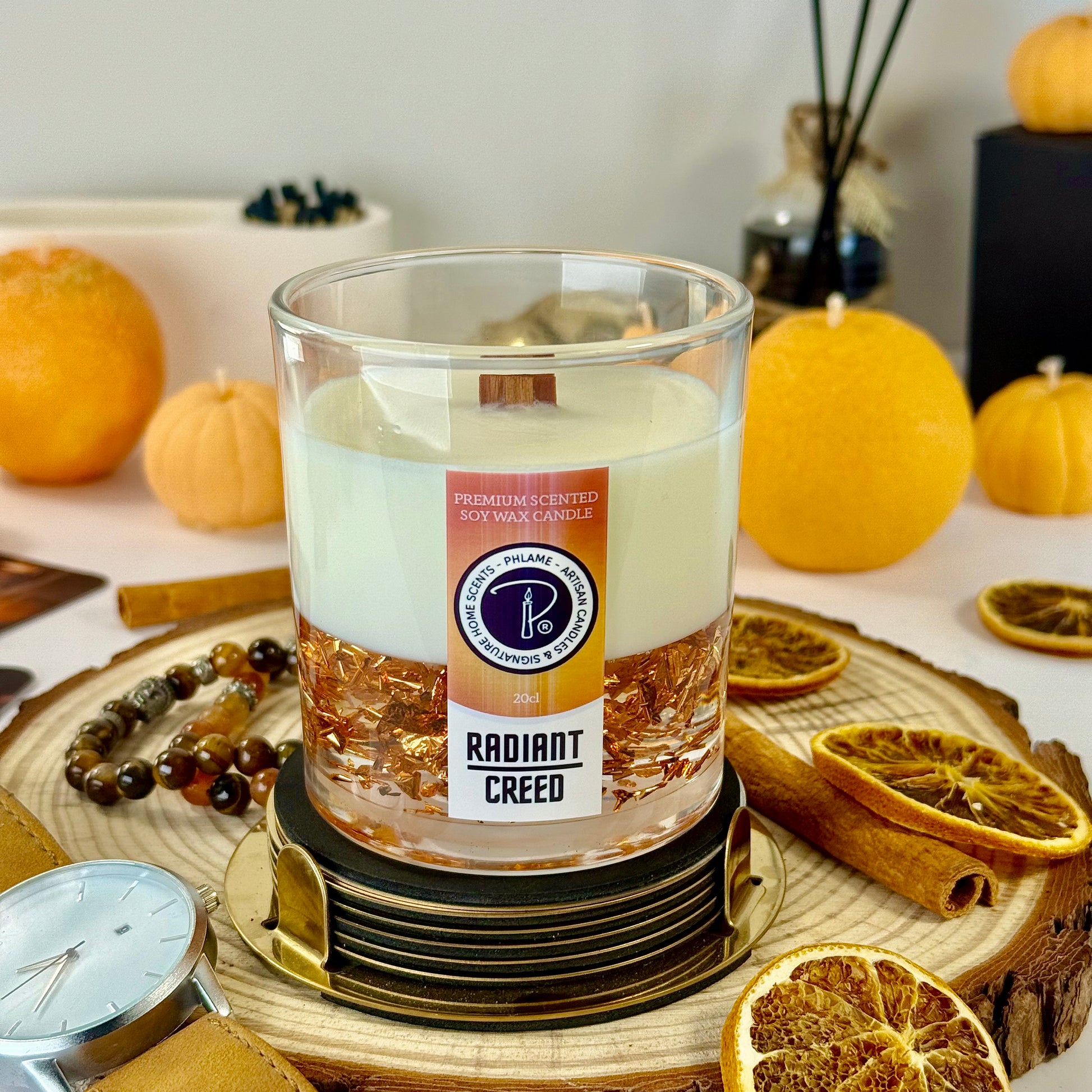 Radiant Creed candle with layered wax and wooden wick in black gift box, styled with citrus and spices.