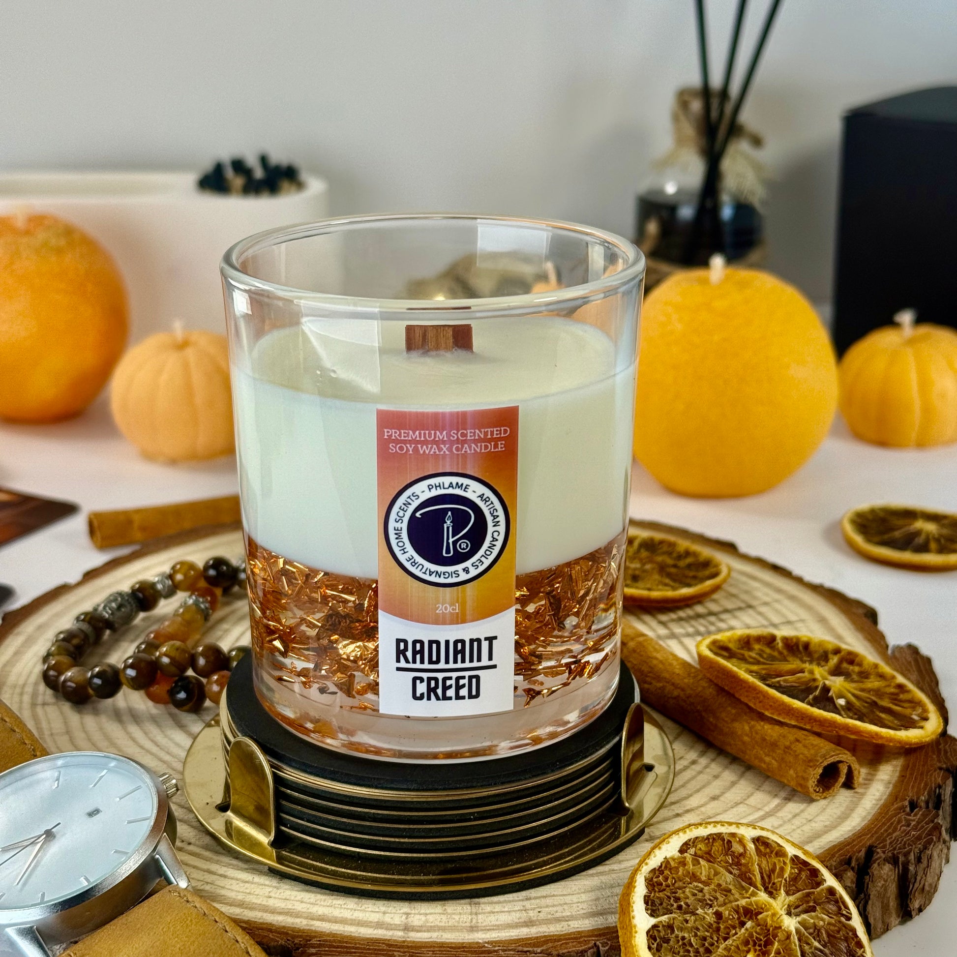Radiant Creed candle with layered wax and wooden wick in black gift box, styled with citrus and spices.