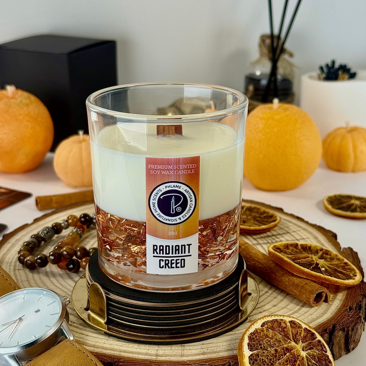 Scented candle labeled 'Radiant Creed' on a decorative surface with dried oranges.