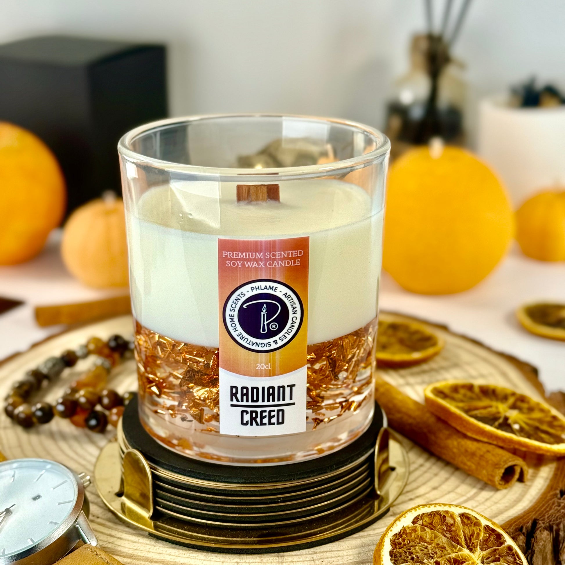 Radiant Creed candle with layered wax and wooden wick in black gift box, styled with citrus and spices.