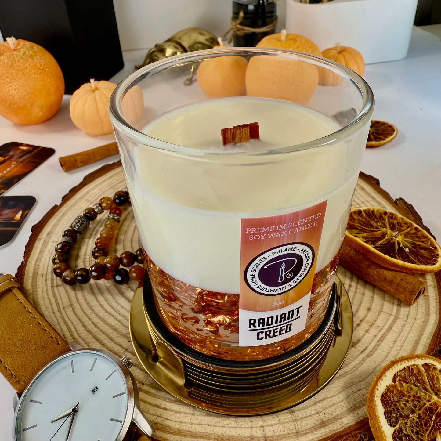 Radiant Creed candle with layered wax and wooden wick in black gift box, styled with citrus and spices.