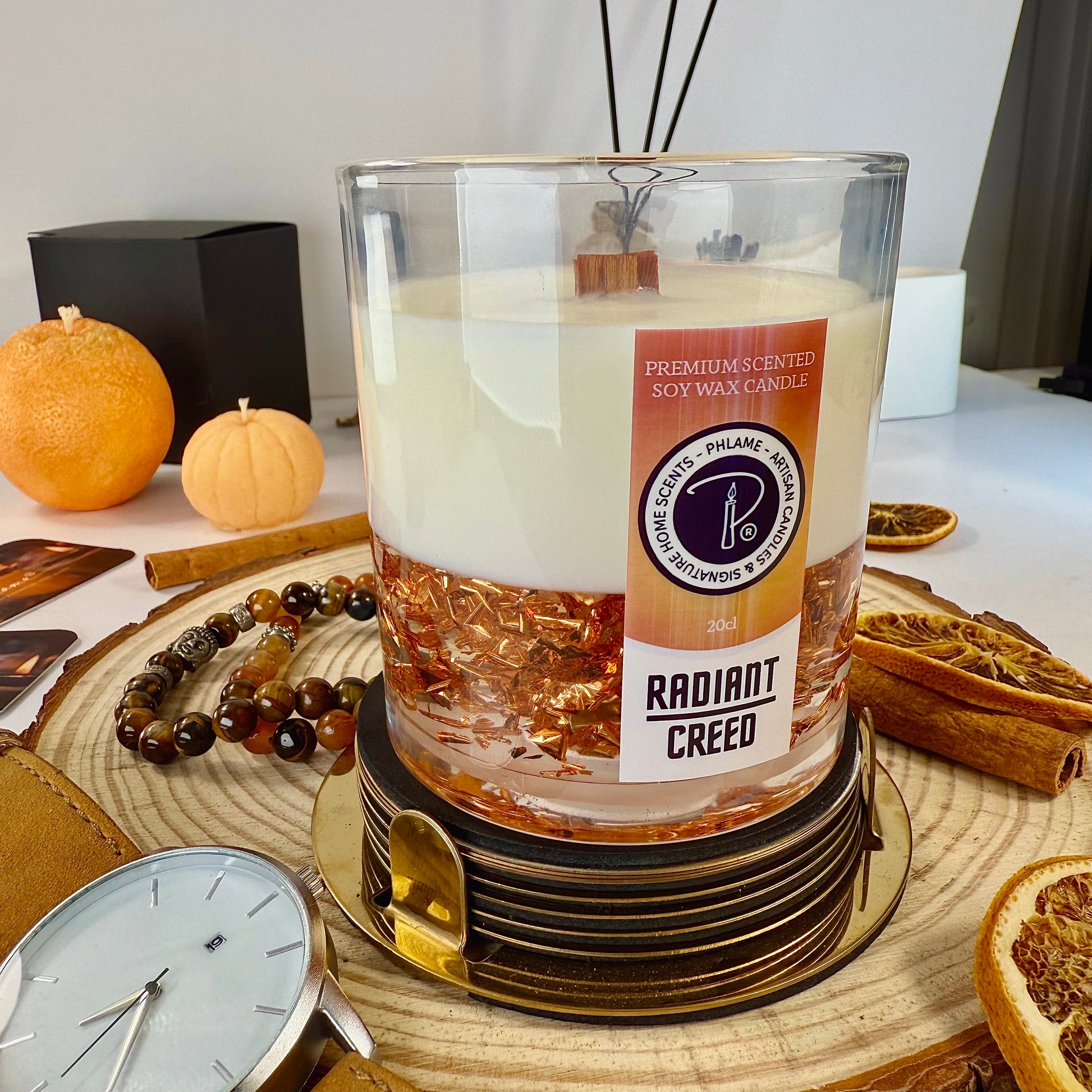Candle labeled 'Radiant Creed' on a coaster with oranges and cinnamon sticks in the background