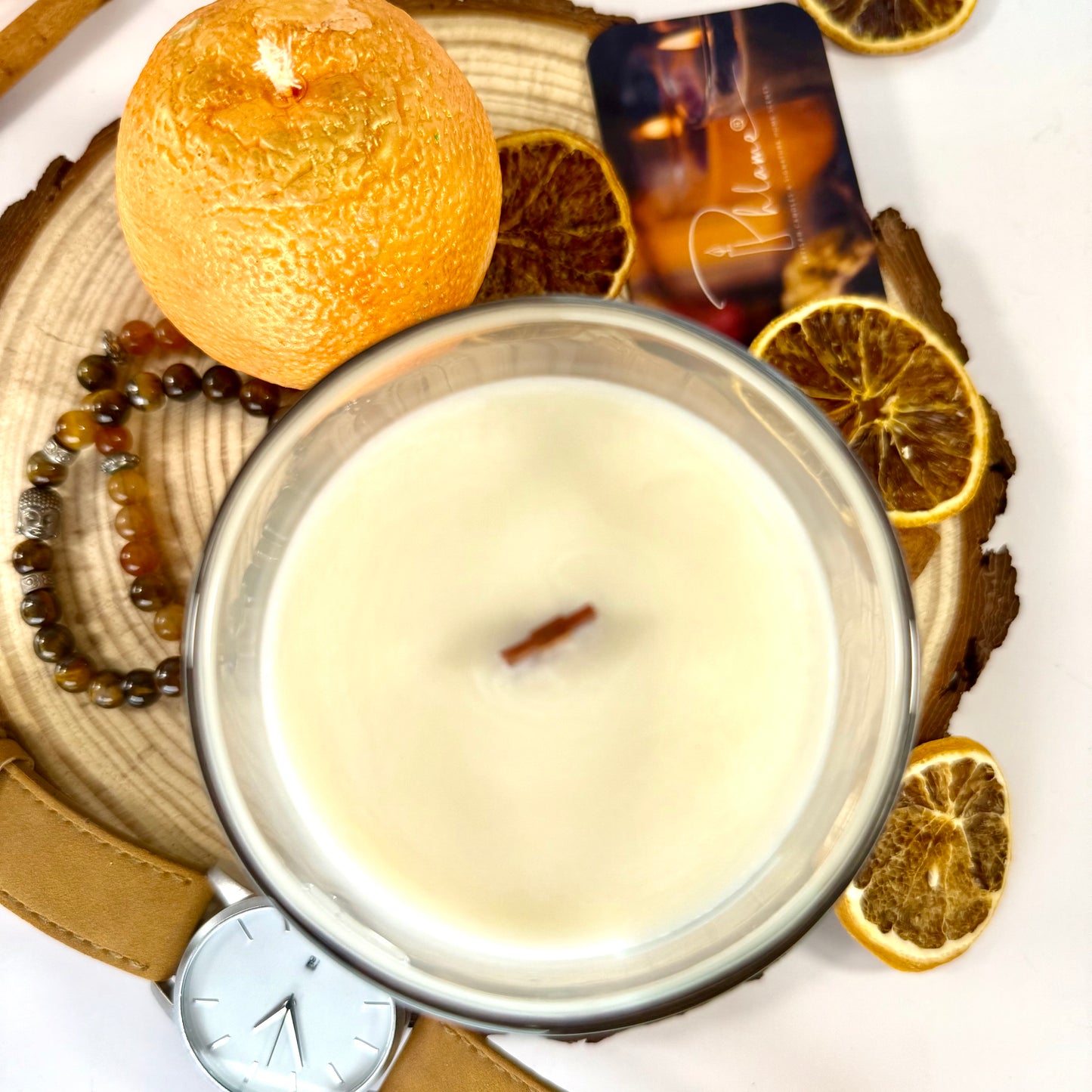 Candle in a glass jar with decorative elements including oranges and a watch on a white background
