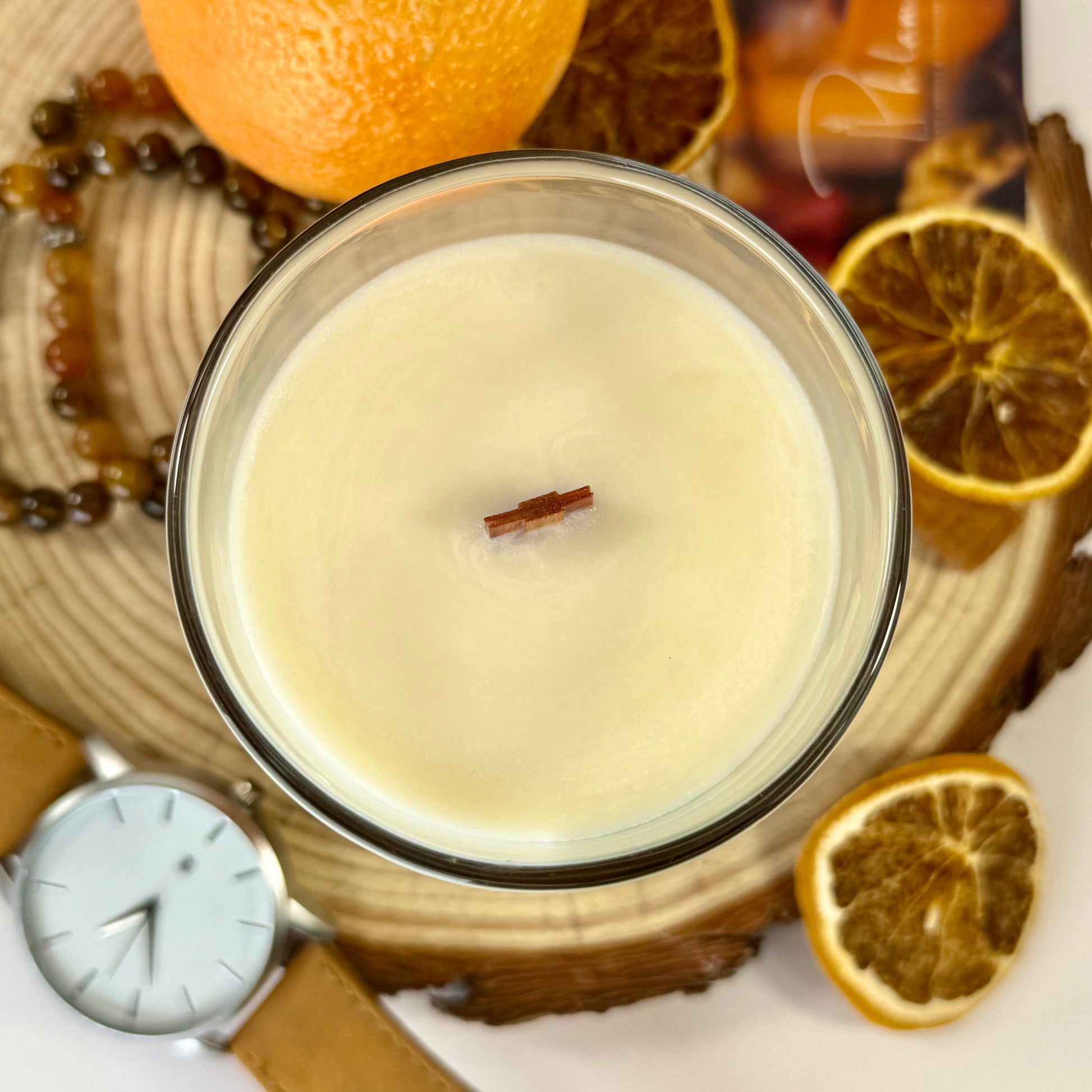 Radiant Creed candle with layered wax and wooden wick in black gift box, styled with citrus and spices.