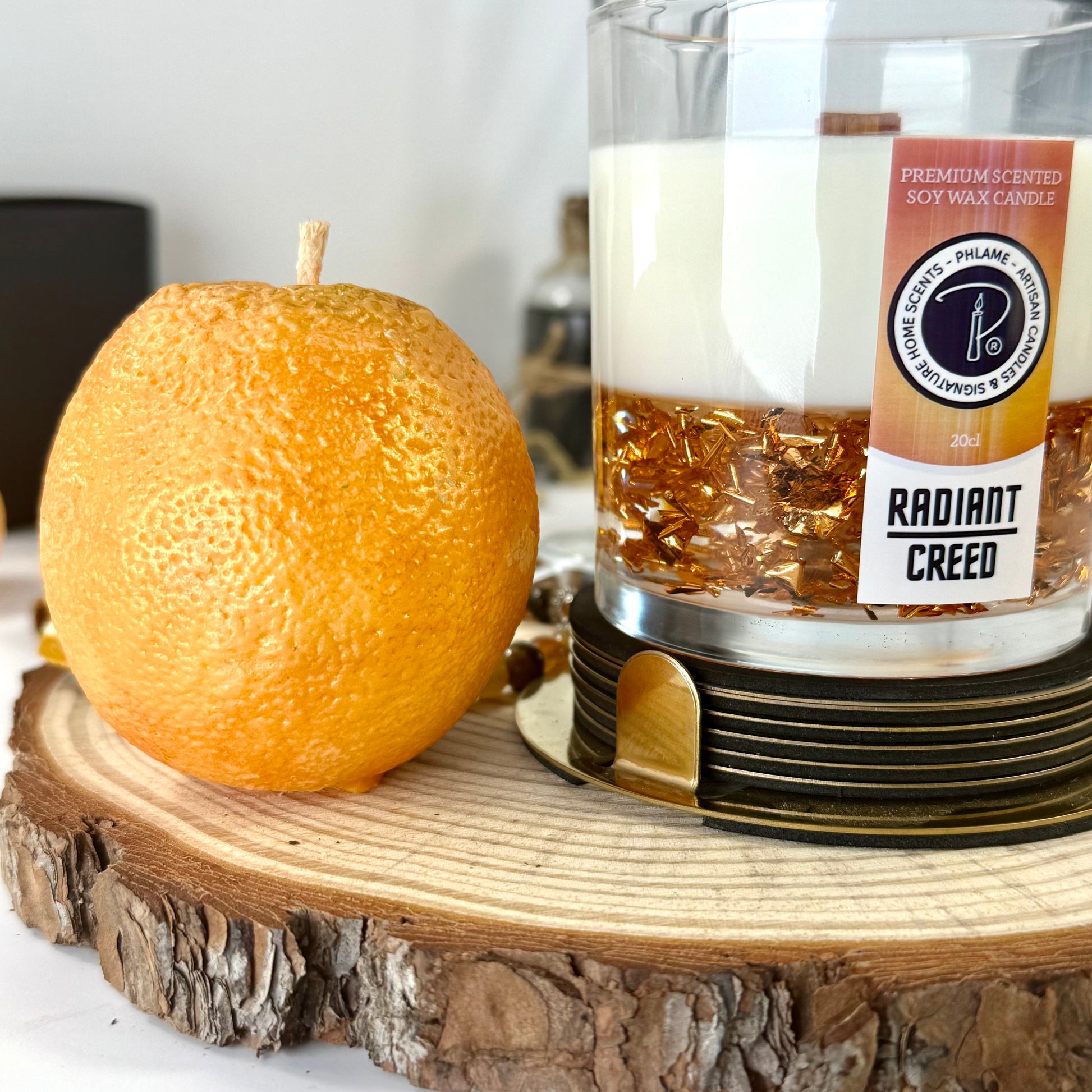 Radiant Creed candle with layered wax and wooden wick in black gift box, styled with citrus and spices.