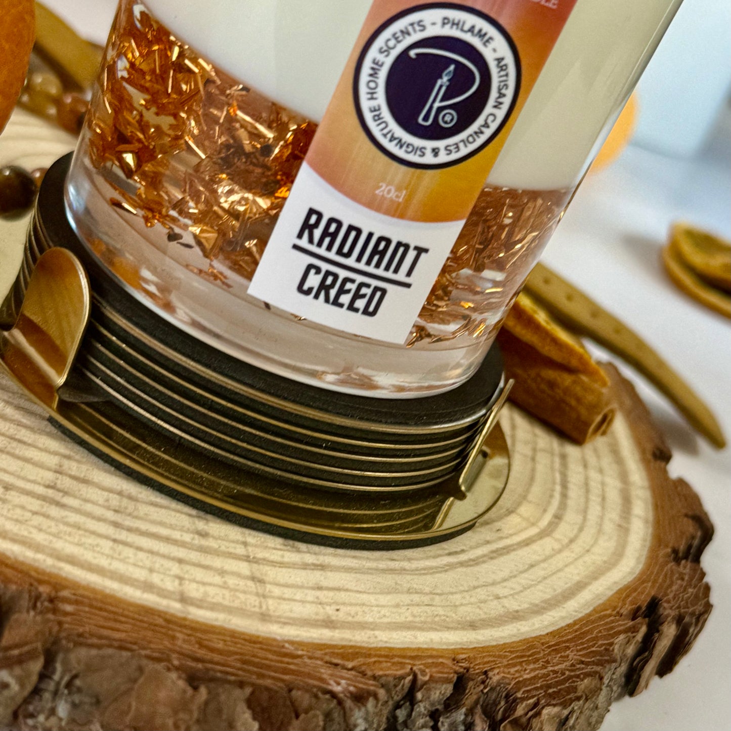 Radiant Creed candle with layered wax and wooden wick in black gift box, styled with citrus and spices.