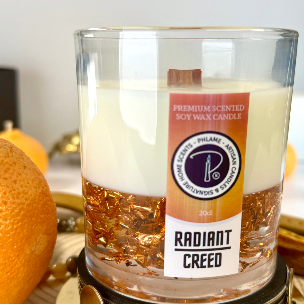 Radiant Creed candle with layered wax and wooden wick in black gift box, styled with citrus and spices.