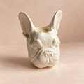 A ceramic French Bulldog head planter in a glossy off-white glaze, set against a warm beige background.
