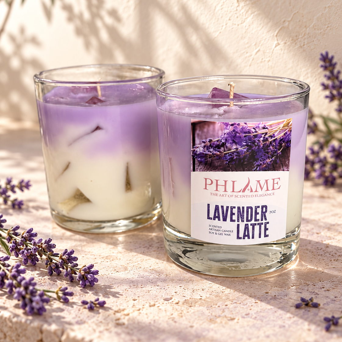Two PHLAME candles in clear glass jars are styled on a stone surface with lavender sprigs and soft shadows. One candle is lavender and white layered, and the front jar has a visible label reading 'PHLAME' and 'LAVENDER LATTE'.
