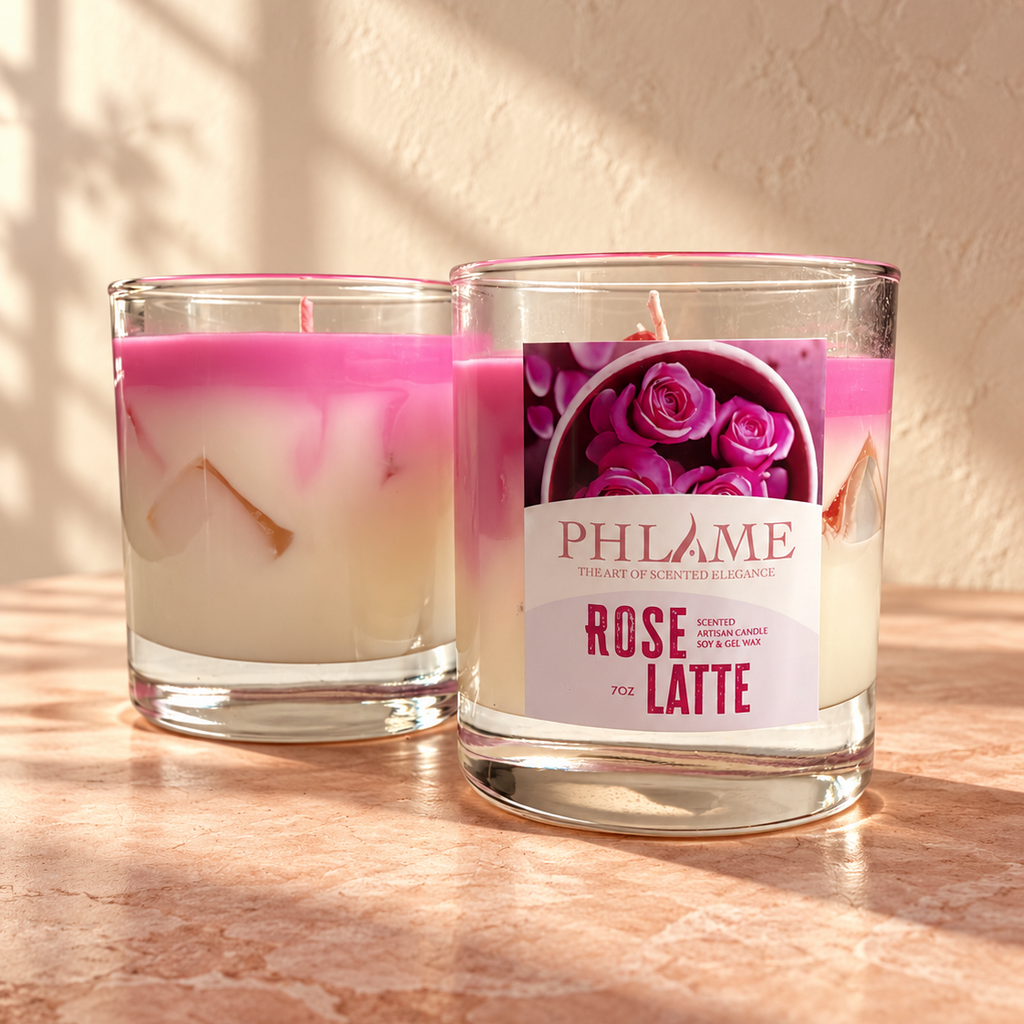 Two PHLAME candles in clear glass jars on a warm stone surface, with one candle showing a pink and white layered wax design and the other displaying a front label that reads PHLAME Rose and Latte.