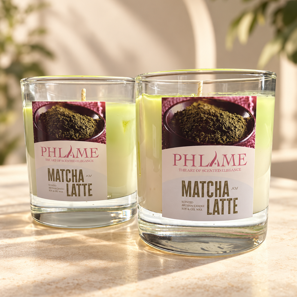 Two PHLAME Matcha and Latte scented candles in clear glass jars, displayed on a warm stone surface with soft, natural background shadows and blurred greenery.