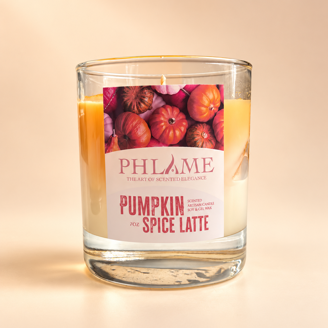 A PHLAME scented candle in a clear glass jar, featuring a label with illustrations of pumpkins and the text 'Pumpkin Spice Latte'. The candle wax is visible through the clear glass, and the background is a soft, warm beige gradient.
