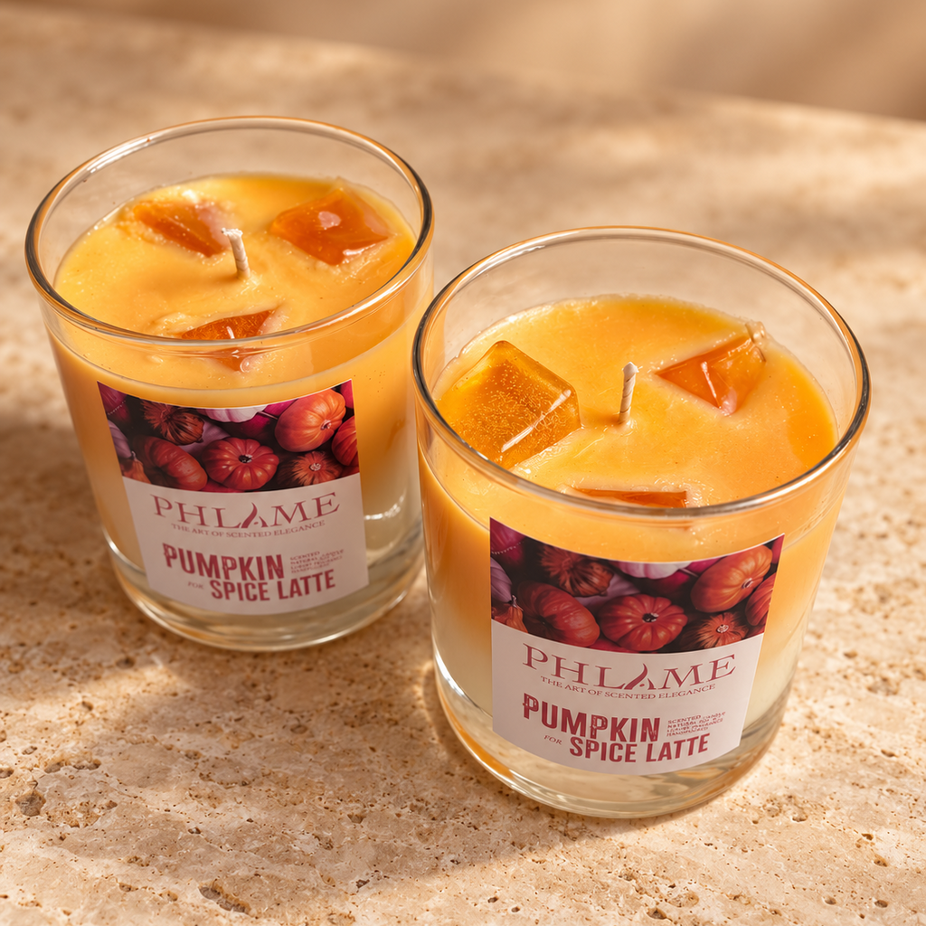 Two PHLAME 'Pumpkin Spice Latte' soy candles in clear glass jars with amber-colored wax and pumpkin illustrations on the labels, set on a textured beige stone surface.