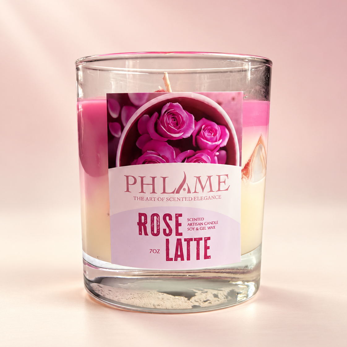 A PHLAME 'Rose Latte' scented candle in a clear glass jar, featuring a pink wax top layer and a cream-colored wax bottom layer, with a label depicting pink roses.