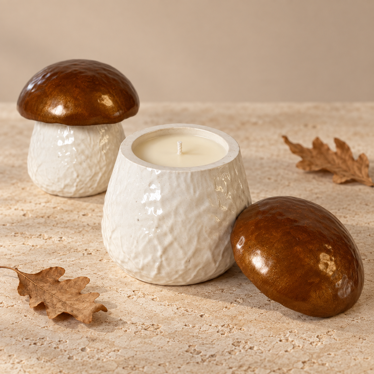 Three ceramic candle holders shaped like mushrooms, with two closed holders and one open holder displaying a cream-colored candle, styled on a textured beige stone surface with dried oak leaves.